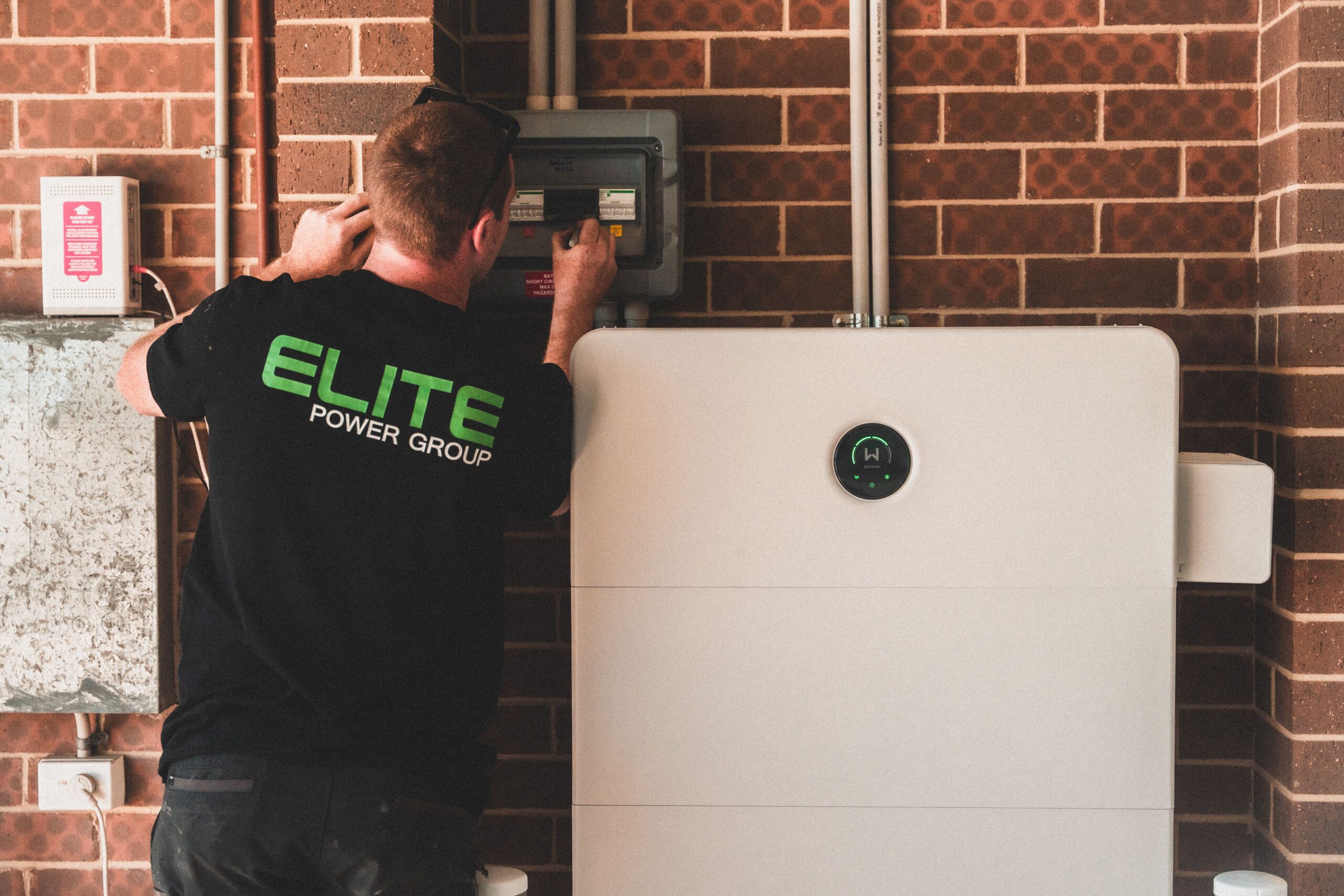 Installed wall-mounted home battery beside a technician and electrical equipment